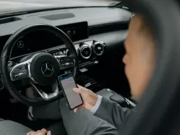 Business Fotografie eines Mannes in einem Auto der ein Smartphone in der Hand hält